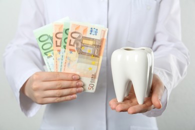 Photo of Dentist holding ceramic model of tooth and euro banknotes on light background, closeup. Expensive treatment