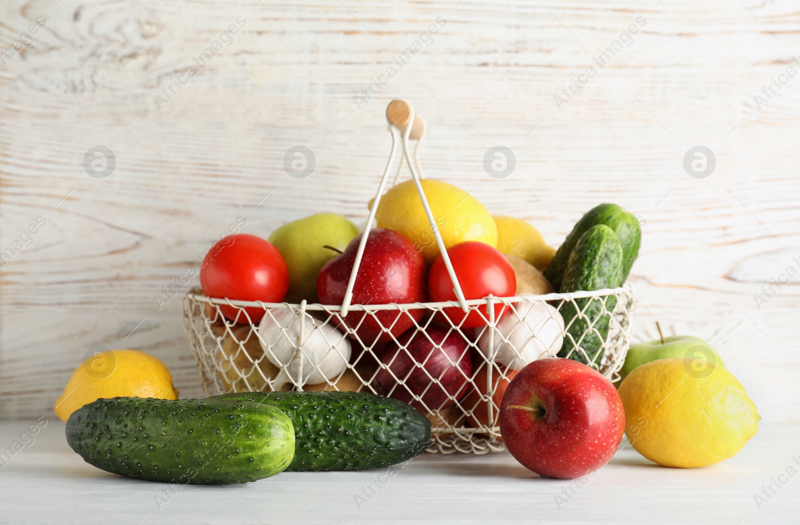 Photo of Basket full of fresh vegetables and fruits on table against wooden background