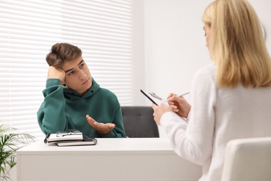 Psychologist working with teenage boy at table in office