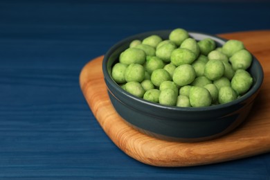Photo of Tasty wasabi coated peanuts in bowl on blue wooden table, closeup. Space for text