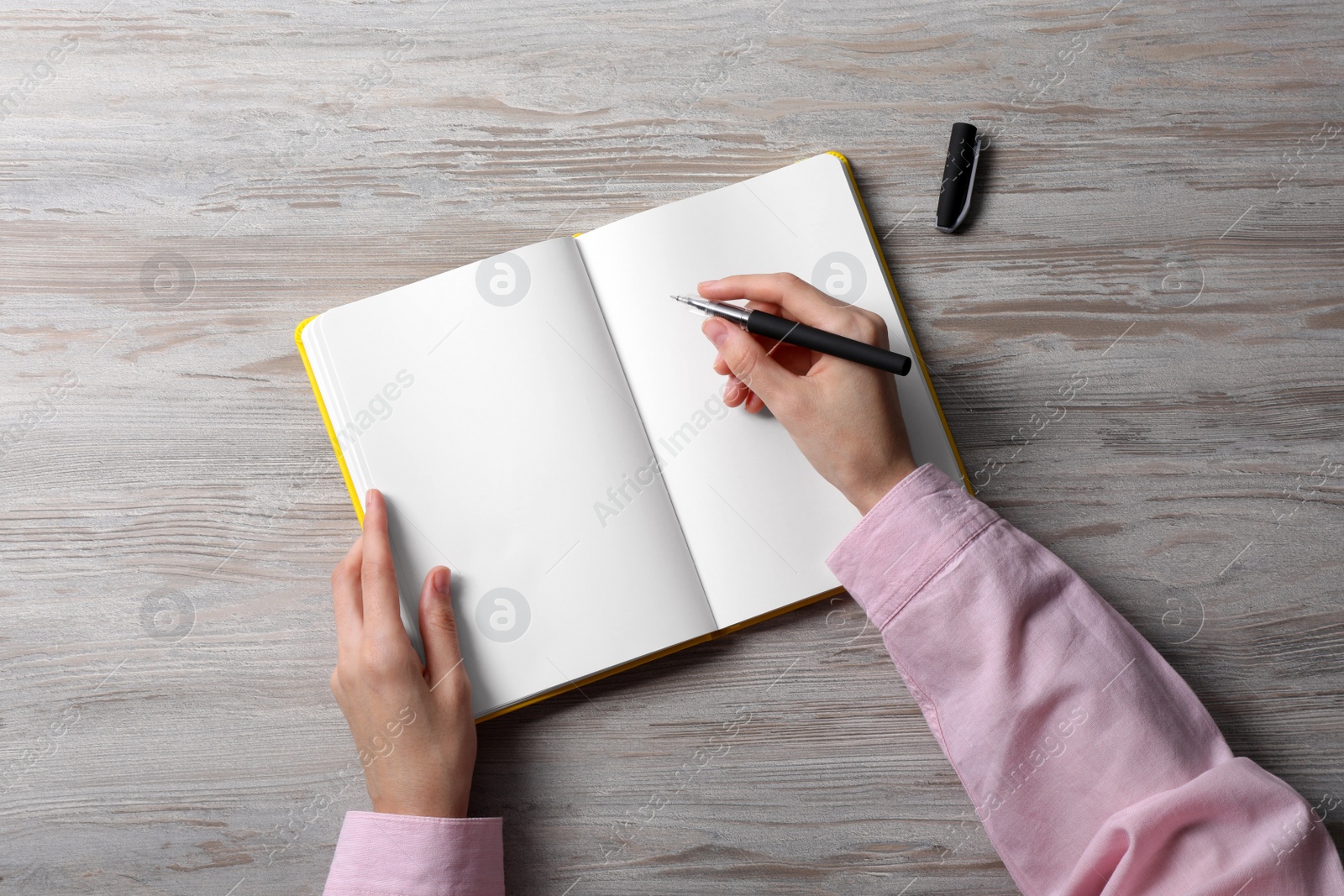 Photo of Woman writing in notebook at white wooden table, top view