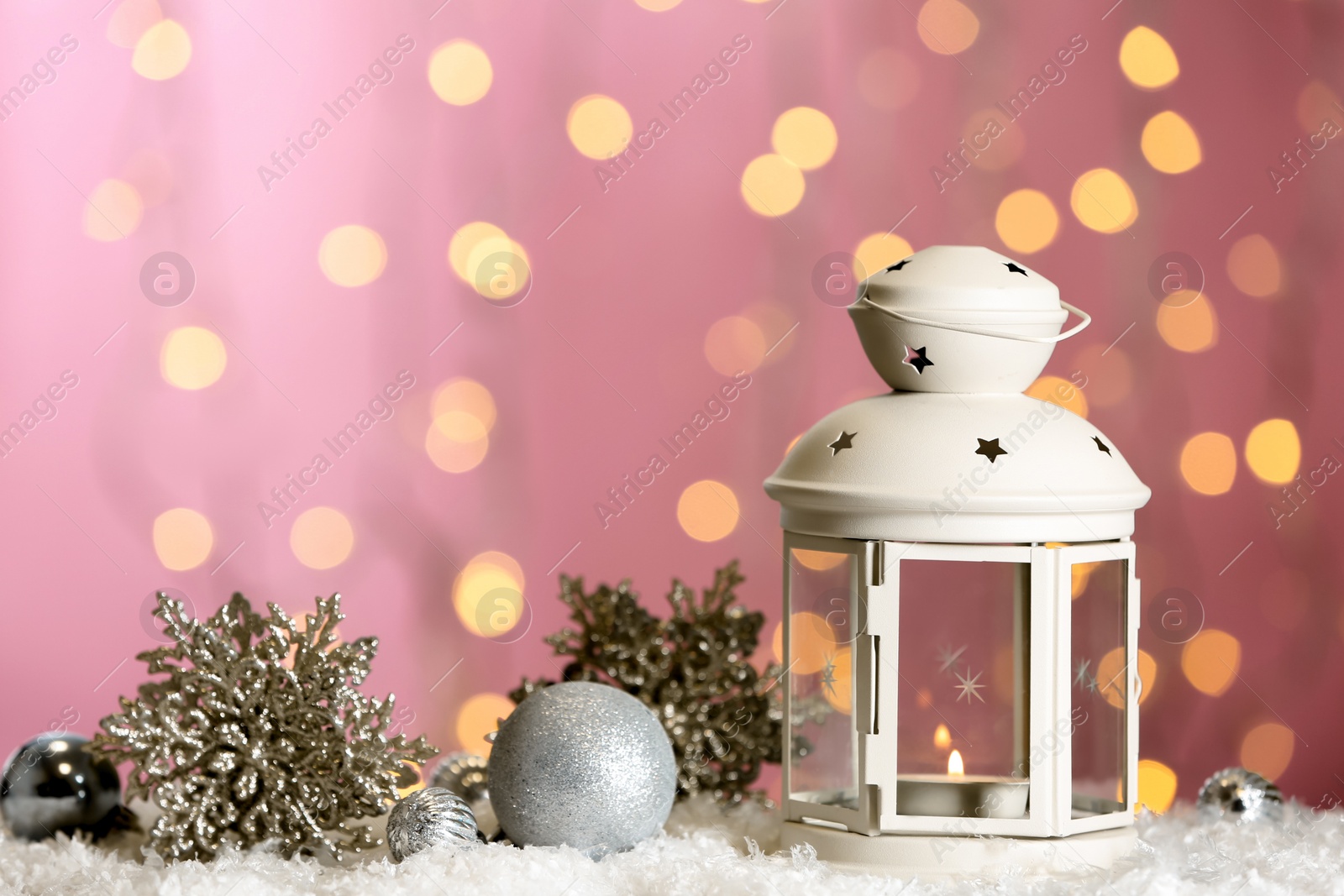 Photo of Christmas lantern with burning candle and festive decor on snow against blurred lights