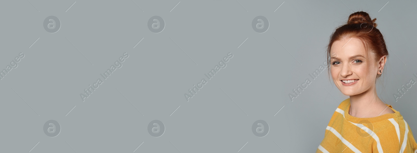 Image of Candid portrait of happy red haired woman with charming smile on grey background, space for text. Horizontal banner design