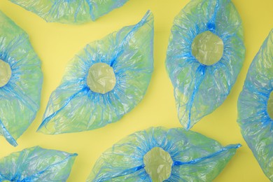 Photo of Blue medical shoe covers on yellow background, flat lay