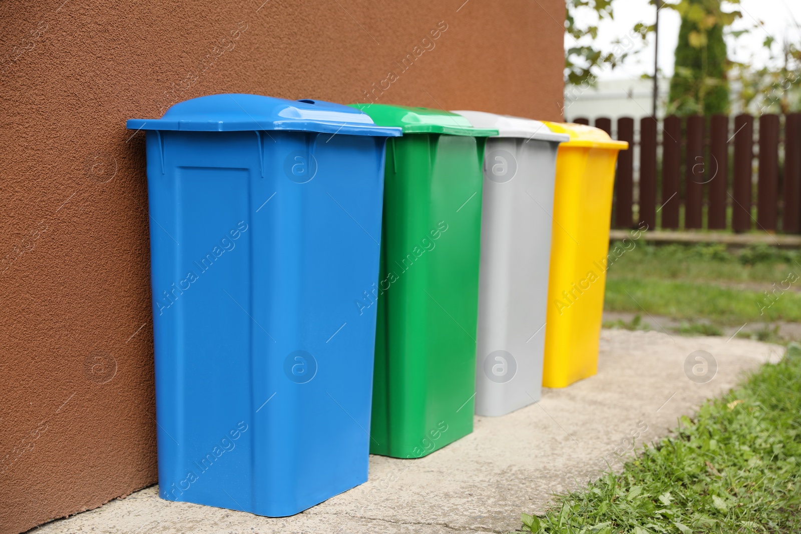 Photo of Many colorful recycling bins near brown wall outdoors