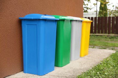 Many colorful recycling bins near brown wall outdoors