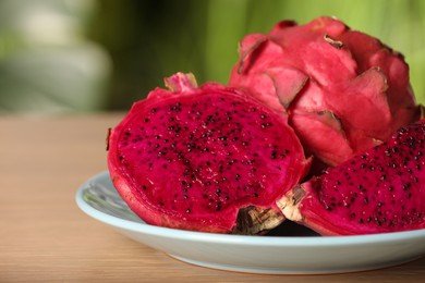 Photo of Plate with delicious cut and whole dragon fruits (pitahaya) on wooden table, closeup