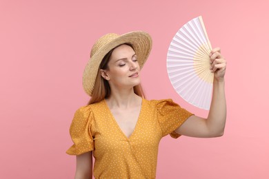 Photo of Beautiful woman waving yellow hand fan to cool herself on pink background