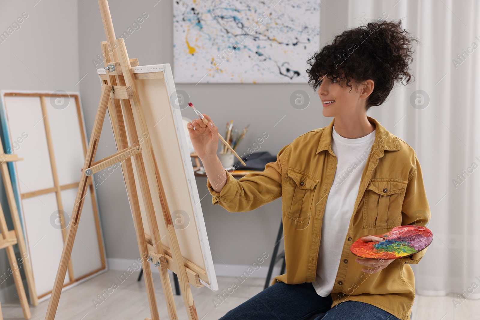 Photo of Young woman painting on easel with canvas in studio