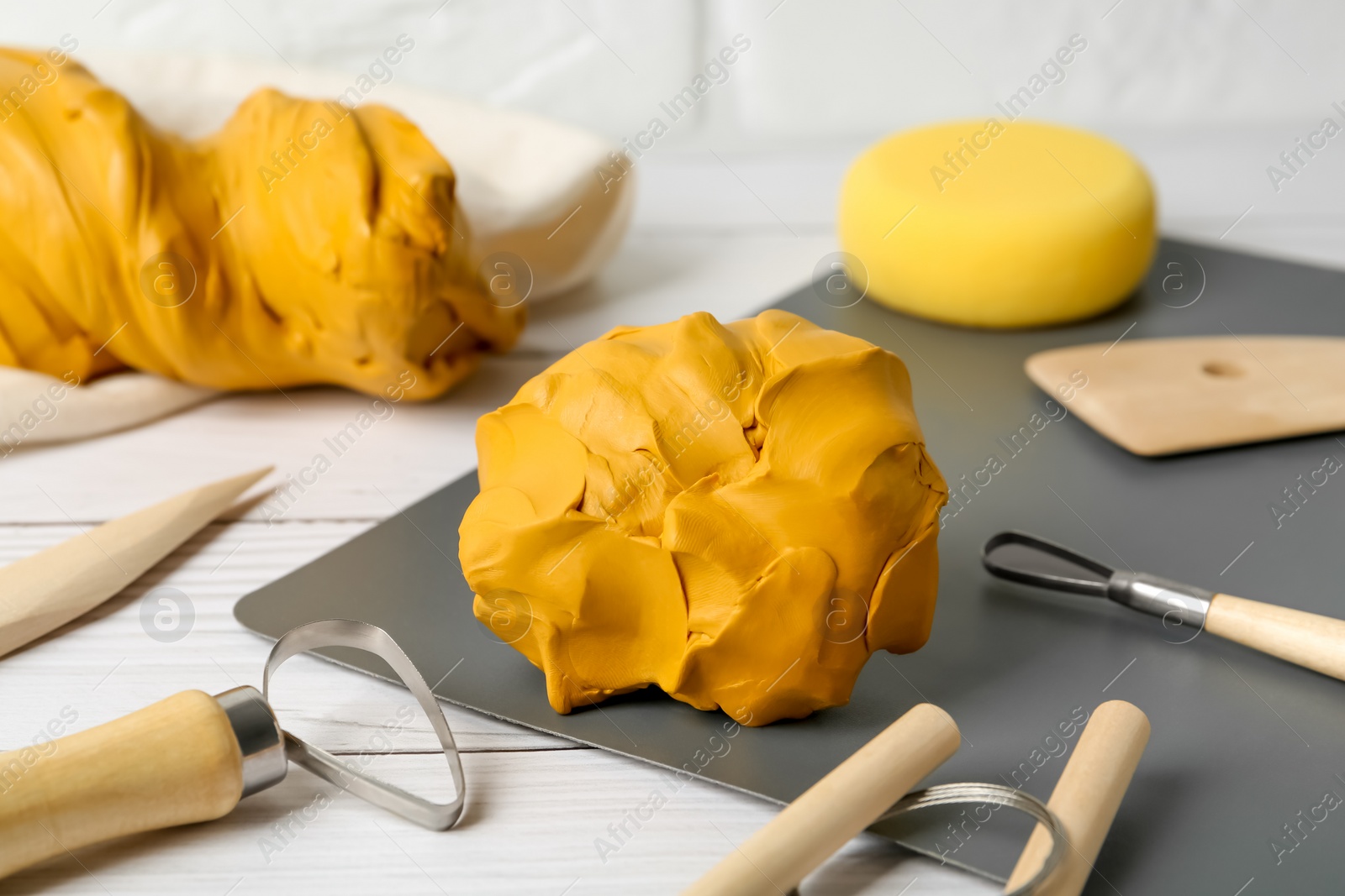 Photo of Clay and set of modeling tools on white wooden table, closeup