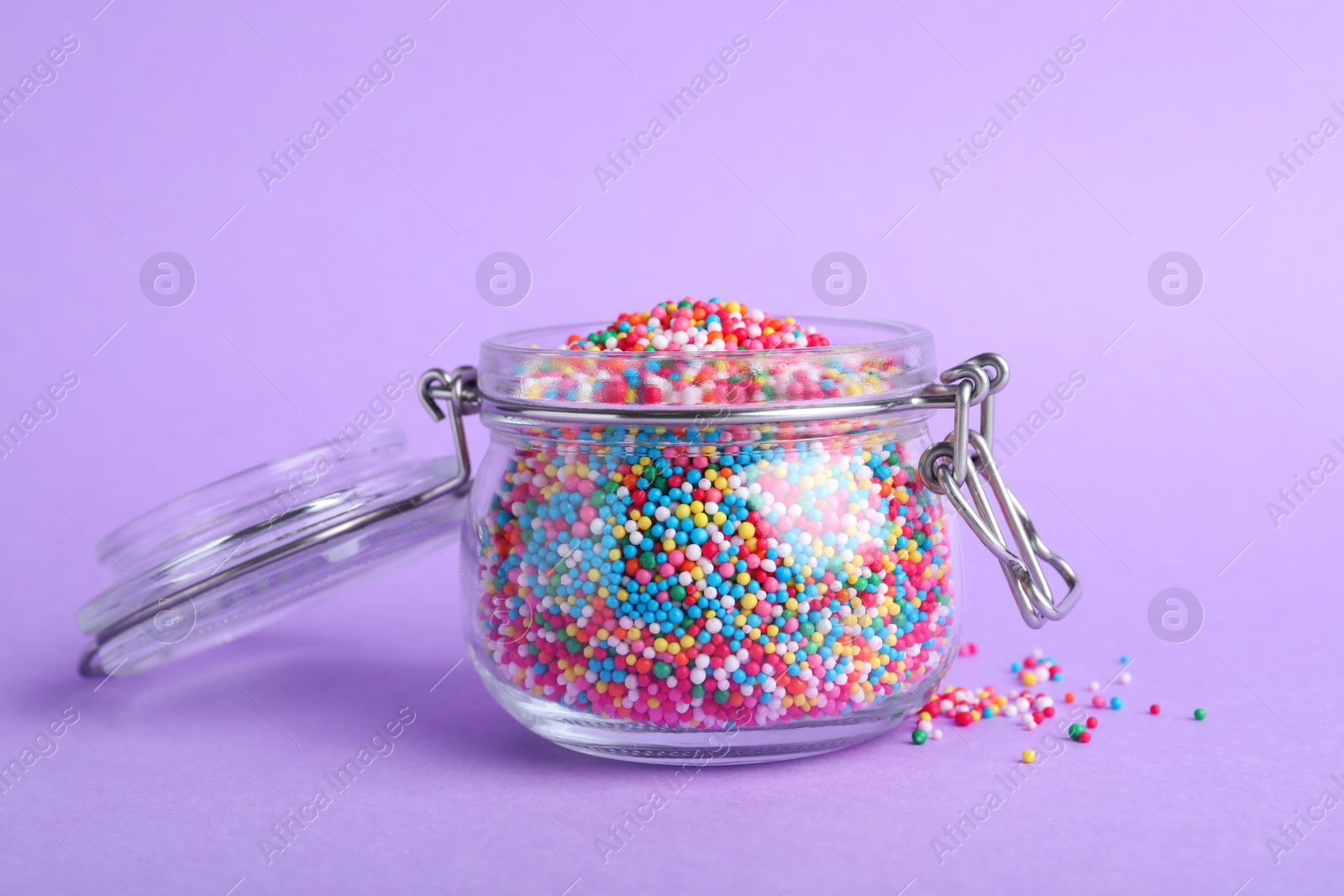 Photo of Colorful sprinkles in jar on lilac background. Confectionery decor