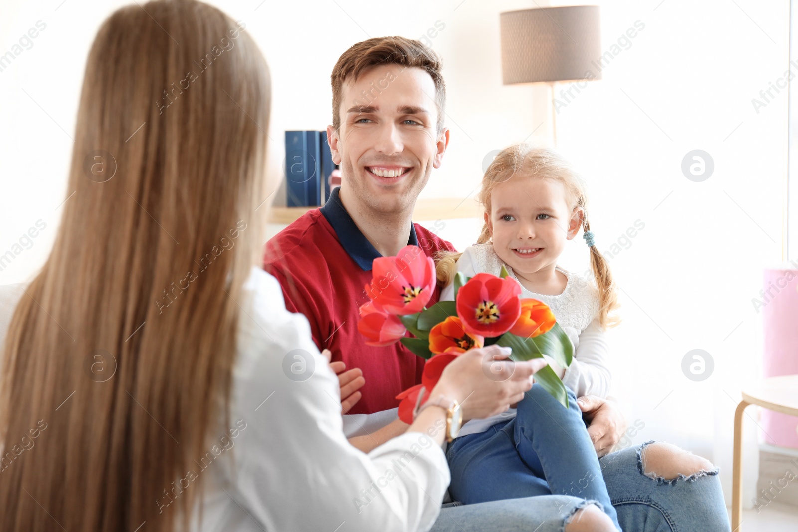 Photo of Happy woman receiving flowers from husband and daughter at home. Mother's day celebration