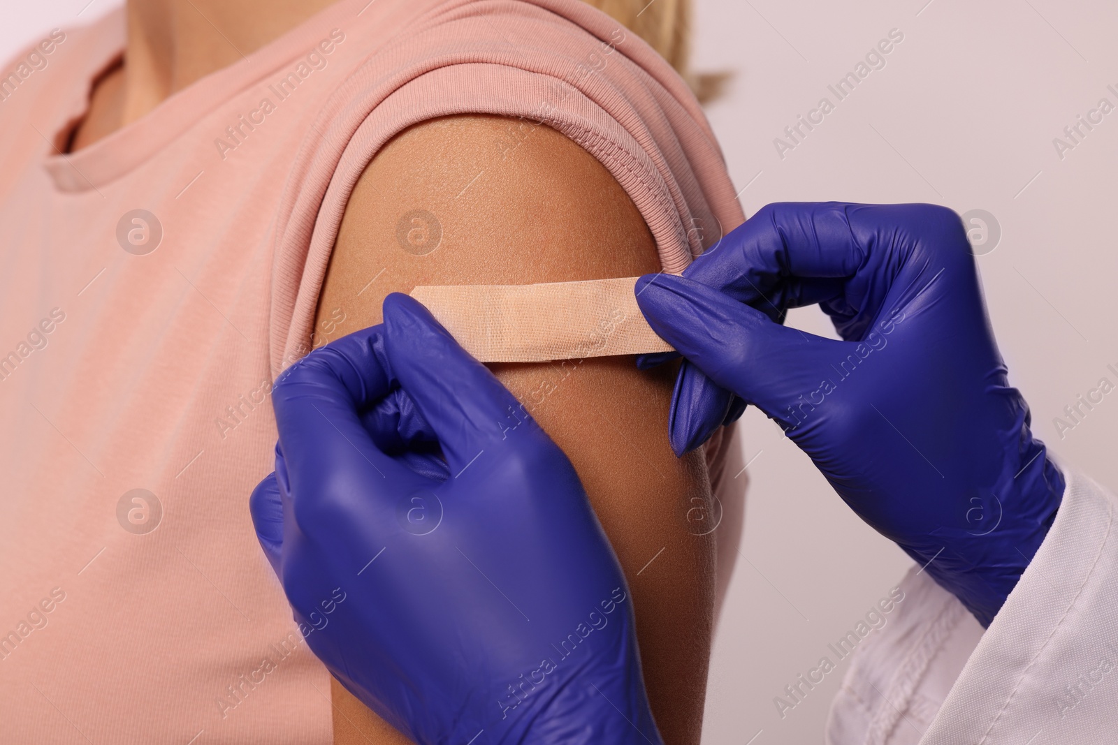 Photo of Nurse sticking adhesive bandage on woman's arm after vaccination on light background, closeup