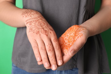 Photo of Woman with henna tattoos on hands against green background, closeup. Traditional mehndi ornament