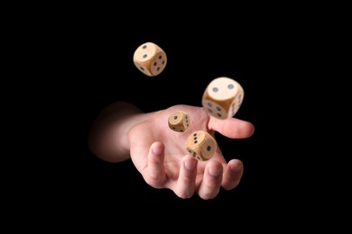 Man throwing wooden dice on black background, closeup