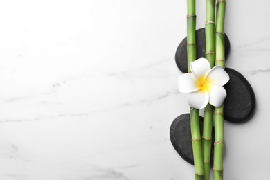 Photo of Spa stones, bamboo stems and plumeria flower on white marble table, flat lay. Space for text