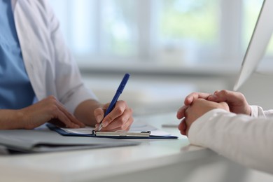 Professional doctor working with patient at white table in hospital, closeup