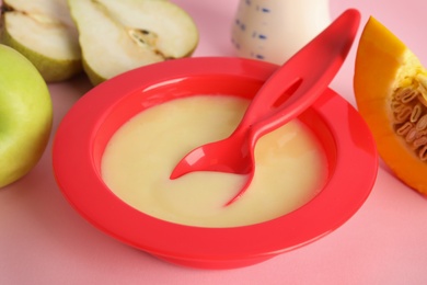 Baby food in bowl and fresh ingredients on pink background