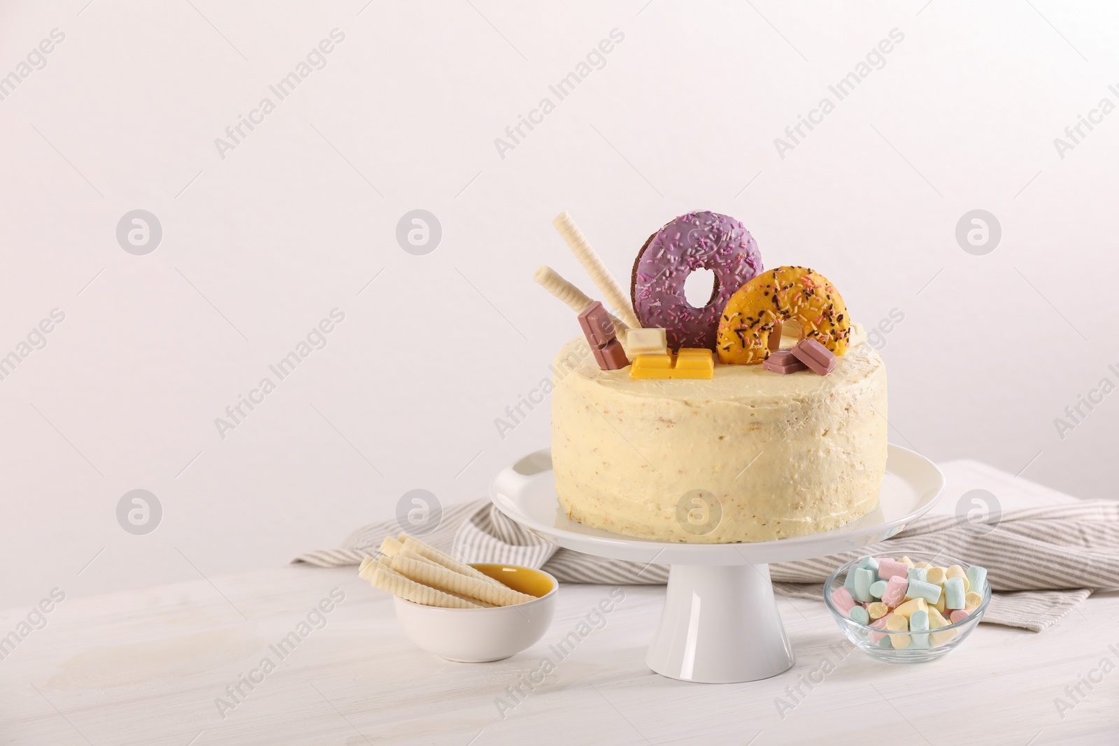 Photo of Delicious cake decorated with sweets, wafer rolls and marshmallows on white wooden table, space for text