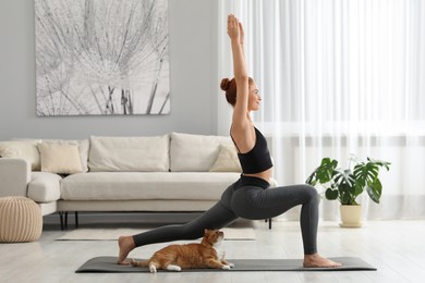 Photo of Young woman with cute red cat practicing yoga on mat at home