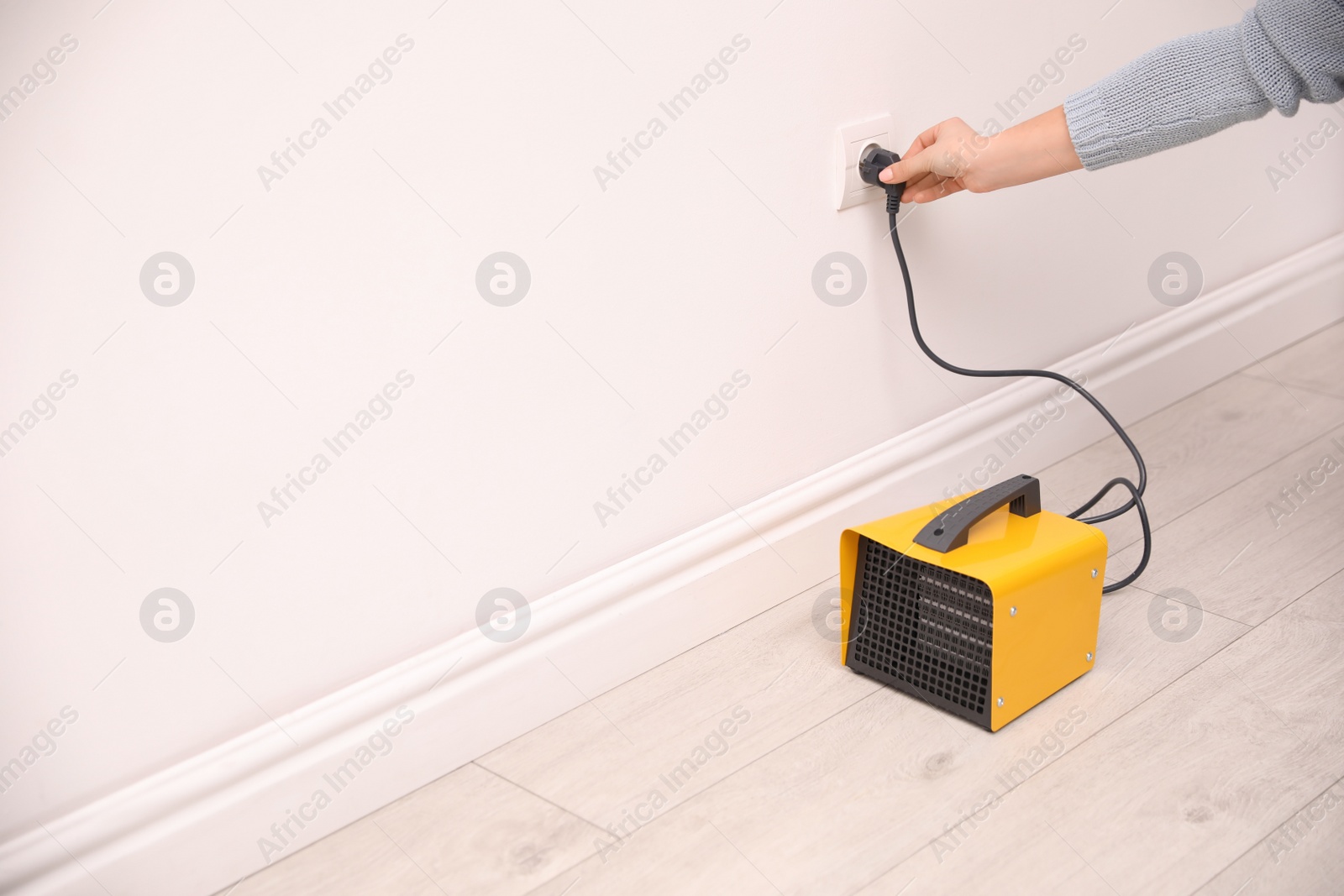 Photo of Woman plug in modern electric fan heater indoors, closeup. Space for text