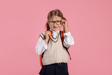 Happy schoolgirl in glasses with backpack on pink background