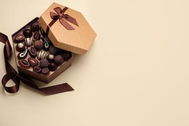 Open box of delicious chocolate candies and brown ribbon on beige background, flat lay. Space for text