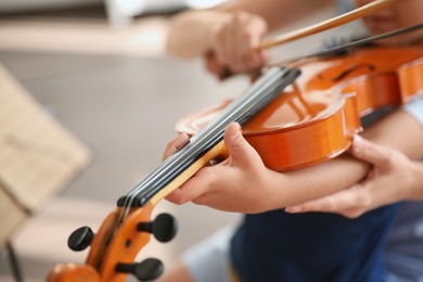 Photo of Young woman teaching little boy to play violin indoors, closeup