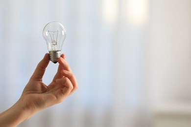 Photo of Woman holding light bulb on blurred background, closeup. Space for text
