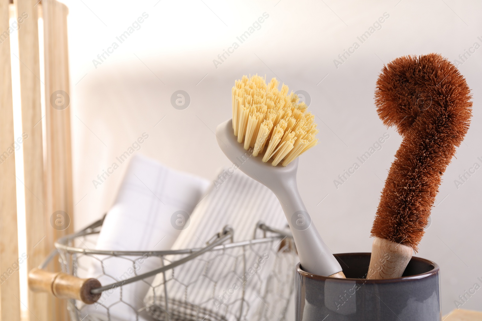 Photo of Cleaning brushes in holder and basket with cloth indoors, closeup