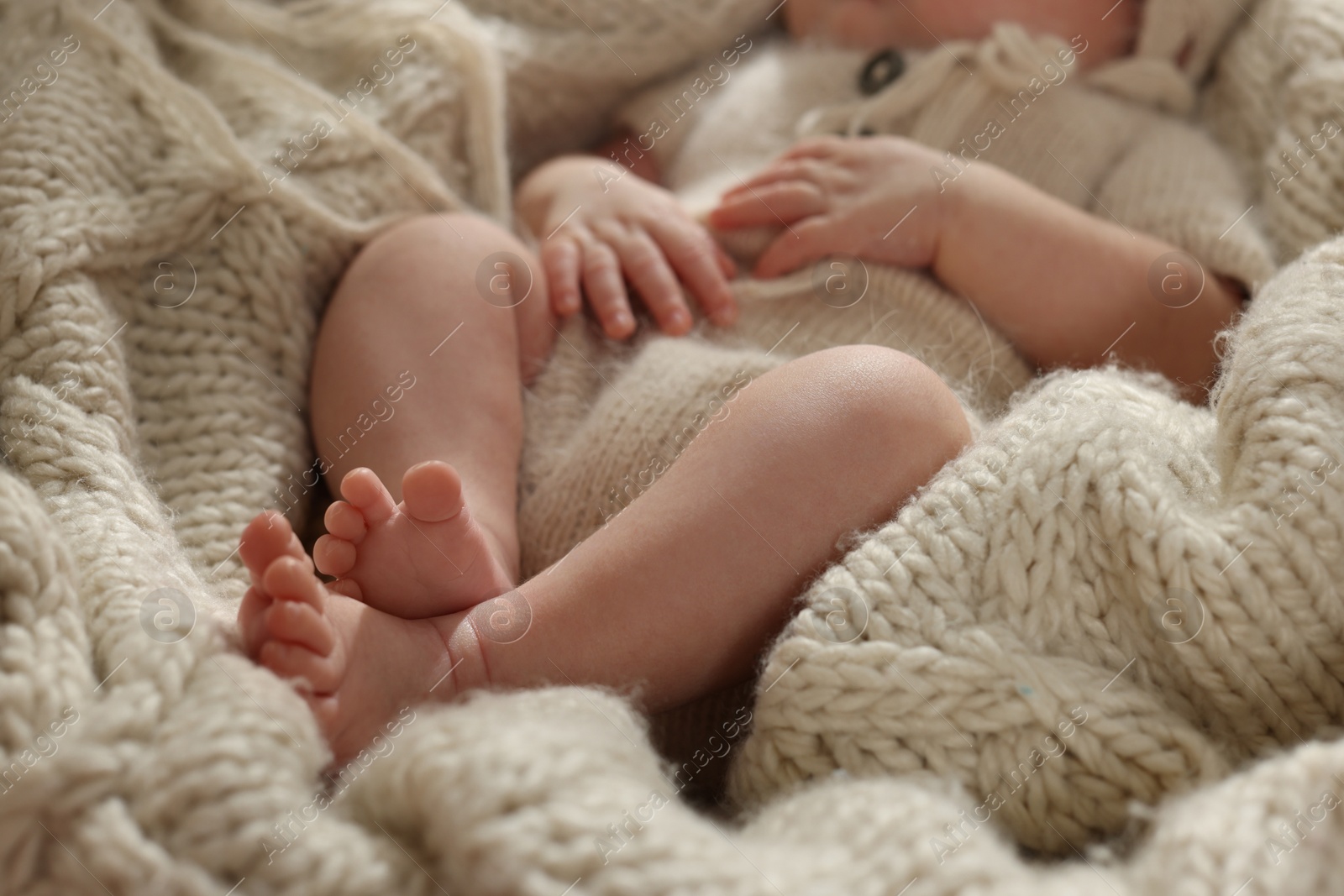 Photo of Adorable newborn baby lying on knitted plaid, closeup