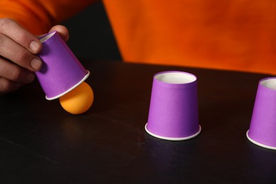Photo of Shell game. Man showing ball under cup at black table, closeup