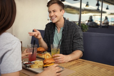 Young happy couple with burgers in street cafe