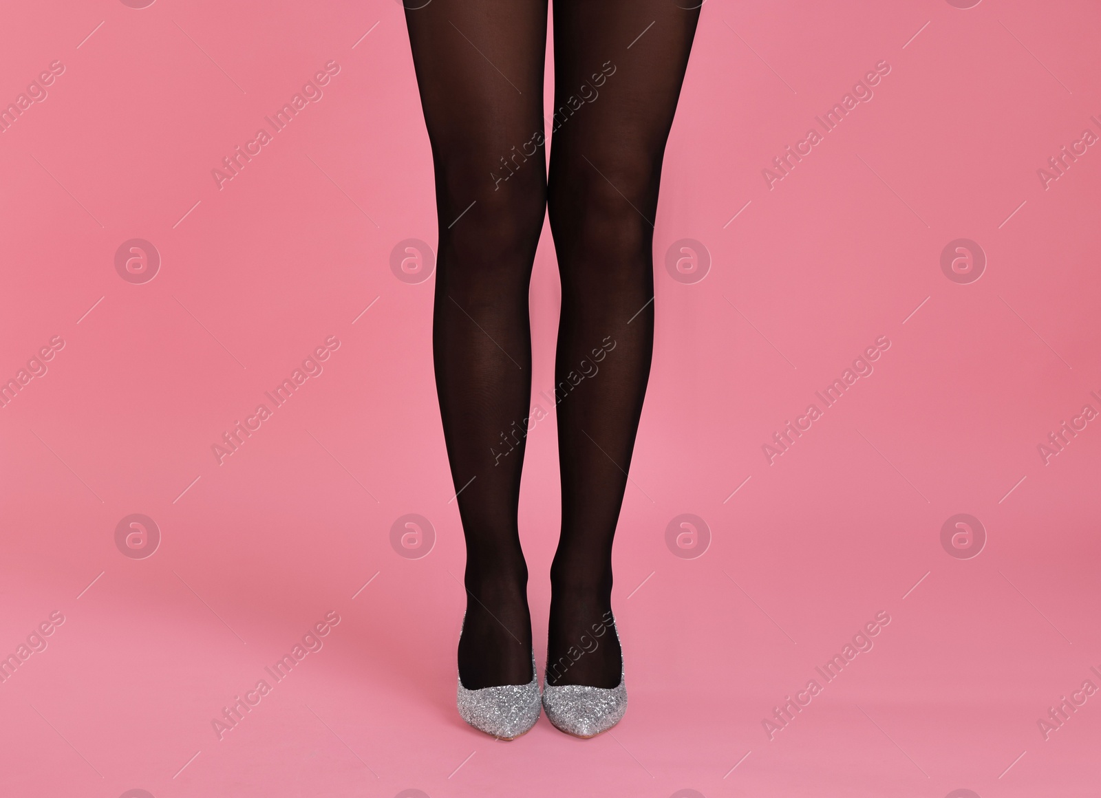 Photo of Woman with beautiful long legs wearing black tights and stylish shoes on pink background, closeup