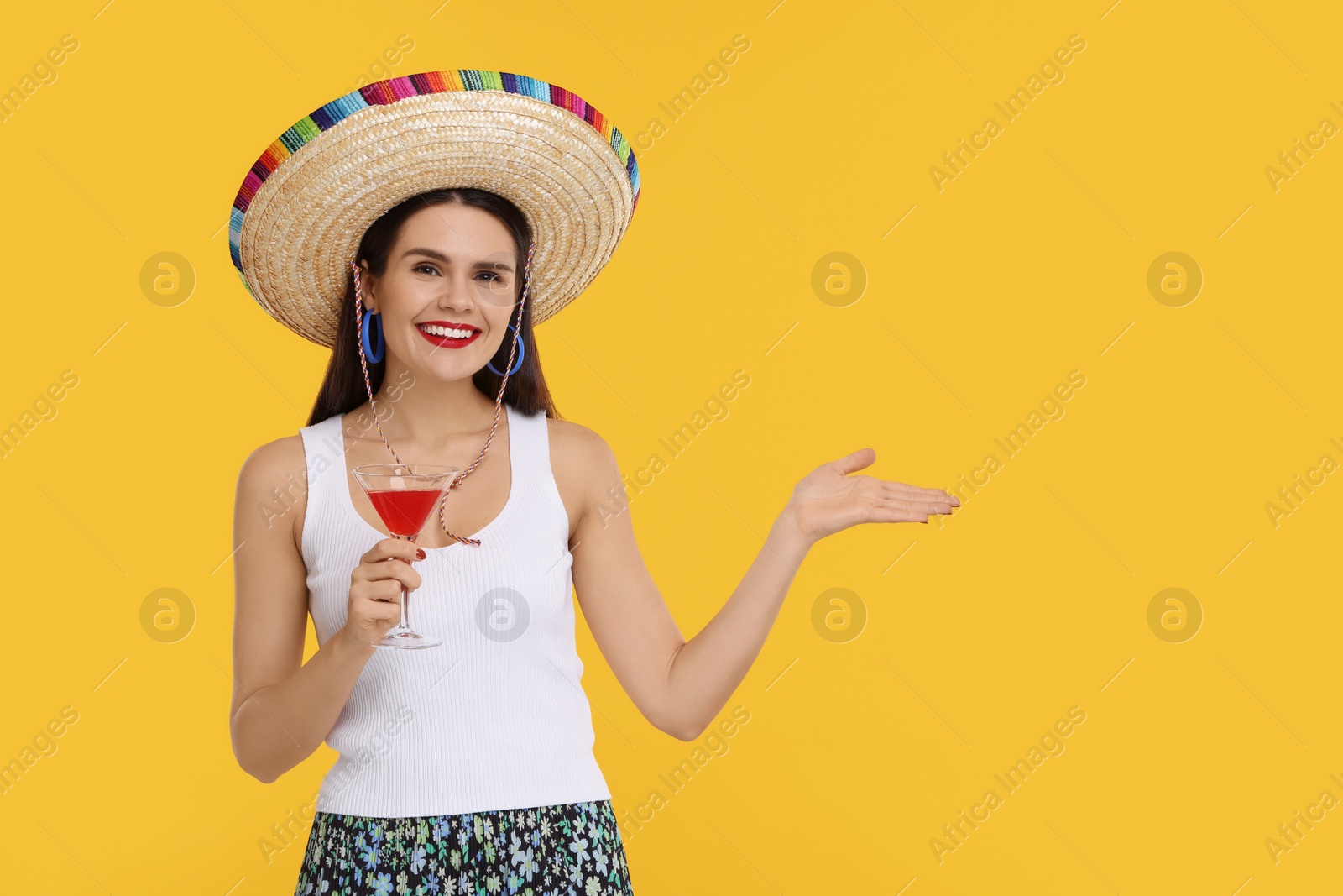 Photo of Young woman in Mexican sombrero hat with cocktail on yellow background. Space for text