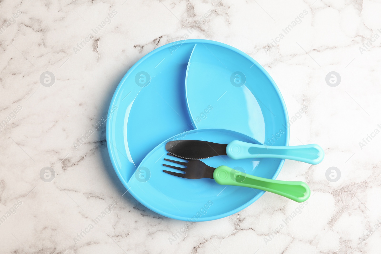 Photo of Section plate with fork and knife on white marble table, top view. Serving baby food