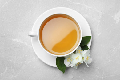 Photo of Cup of tea and fresh jasmine flowers on light grey marble table, top view