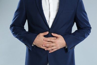 Man in office suit suffering from stomach ache on grey background, closeup. Food poisoning