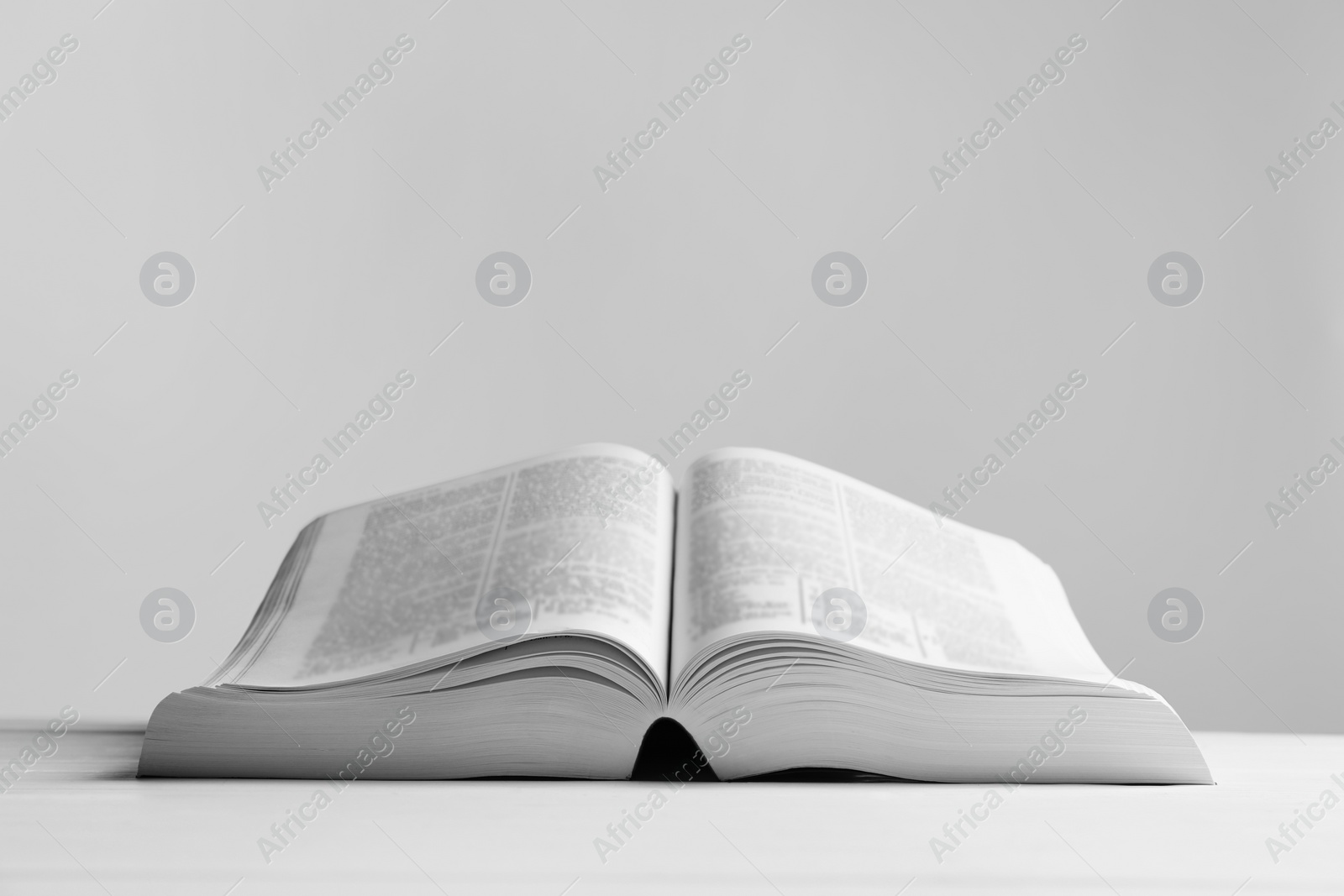 Photo of Open Bible on white wooden table, space for text. Religious book