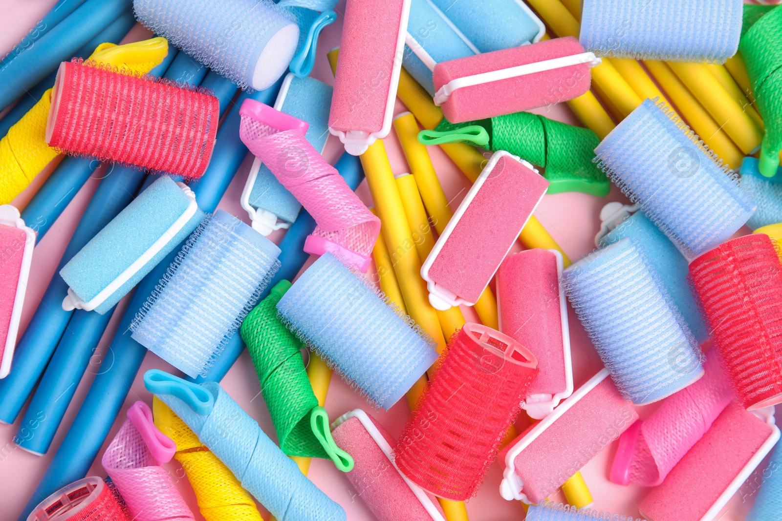 Photo of Many different hair curlers on pink background, flat lay