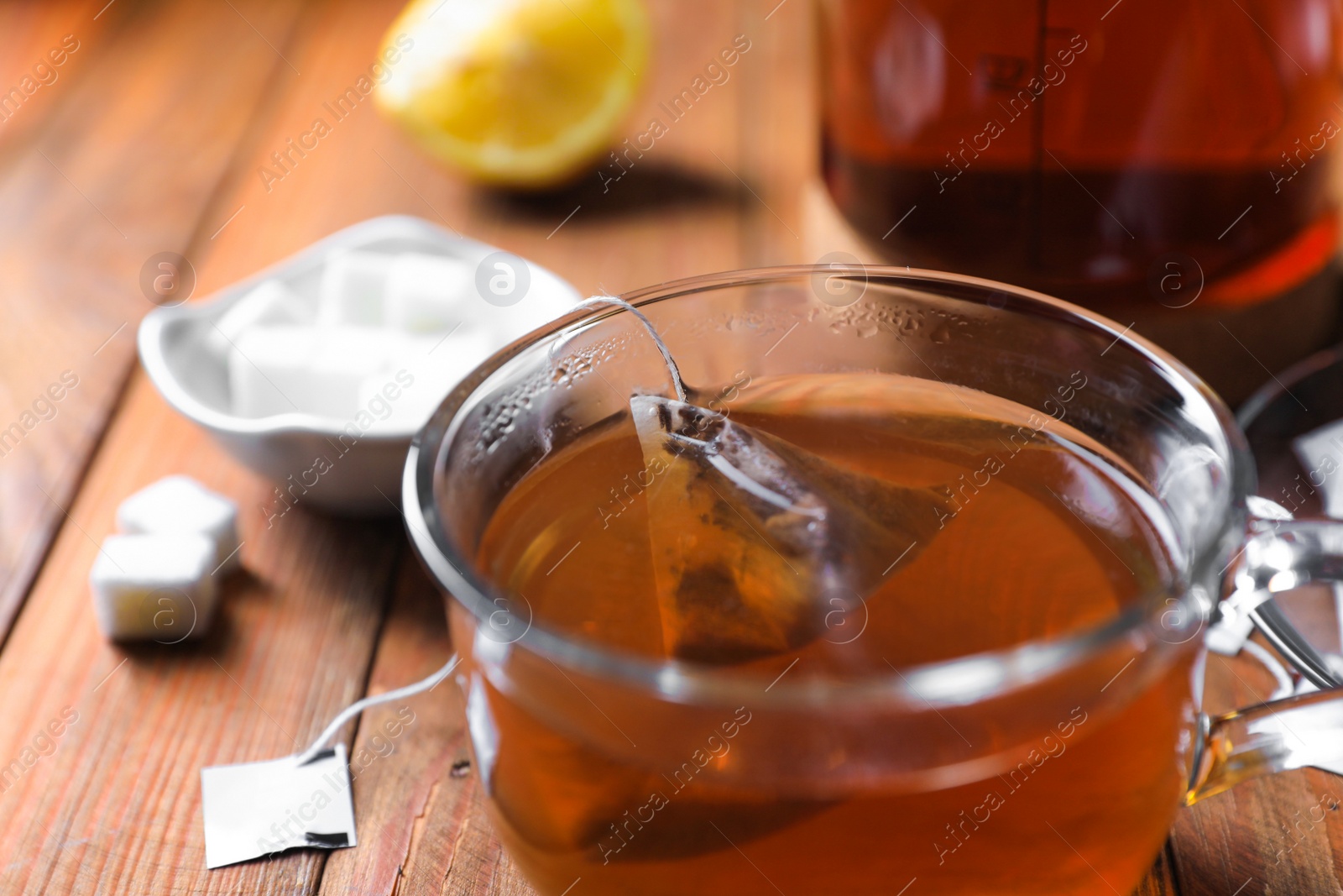 Photo of Tea bag in glass cup on wooden table, closeup