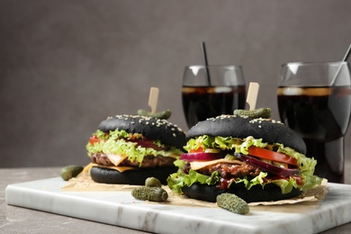 Photo of Board with black burgers and drinks served on table
