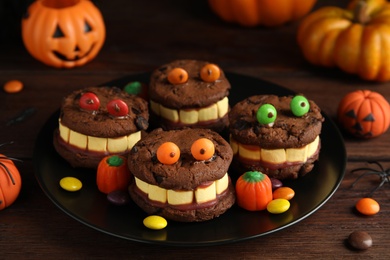 Photo of Delicious desserts decorated as monsters on wooden table. Halloween treat