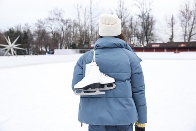 Image of Woman with figure skates near ice rink outdoors, back view