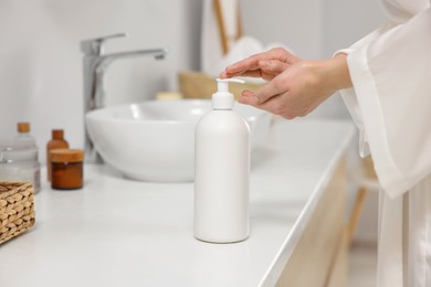 Young woman using body cream in bathroom, closeup