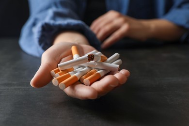 Stop smoking. Woman holding whole and broken cigarettes at black table, closeup