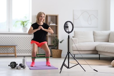 Smiling sports blogger streaming online fitness lesson with smartphone at home