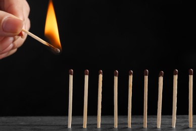 Photo of Woman igniting line of matches on table against dark background, closeup. Space for text