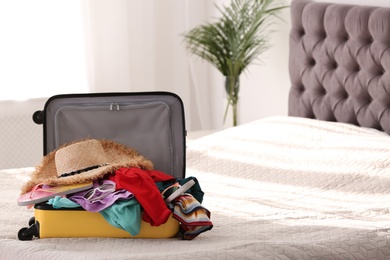 Modern suitcase full of clothes on bed indoors. Space for text