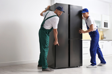 Professional workers carrying modern refrigerator in kitchen